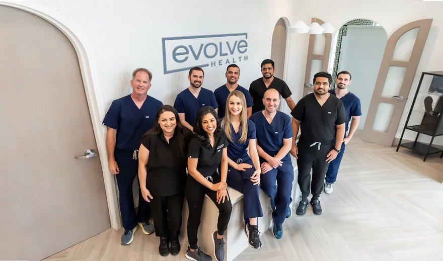 The Evolve Health team standing together in a clinic beneath the Evolve Health logo.