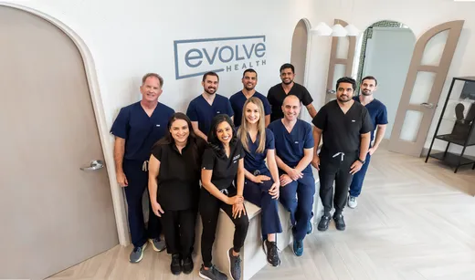 The Evolve Health team standing together in a clinic beneath the Evolve Health logo.